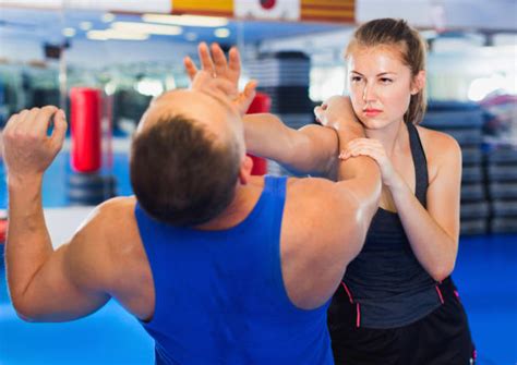 Training A woman in training gear is hitting the chin of a man with the heel of her hand. They are in a gymnasium; she is showing determination and resolve on her face.